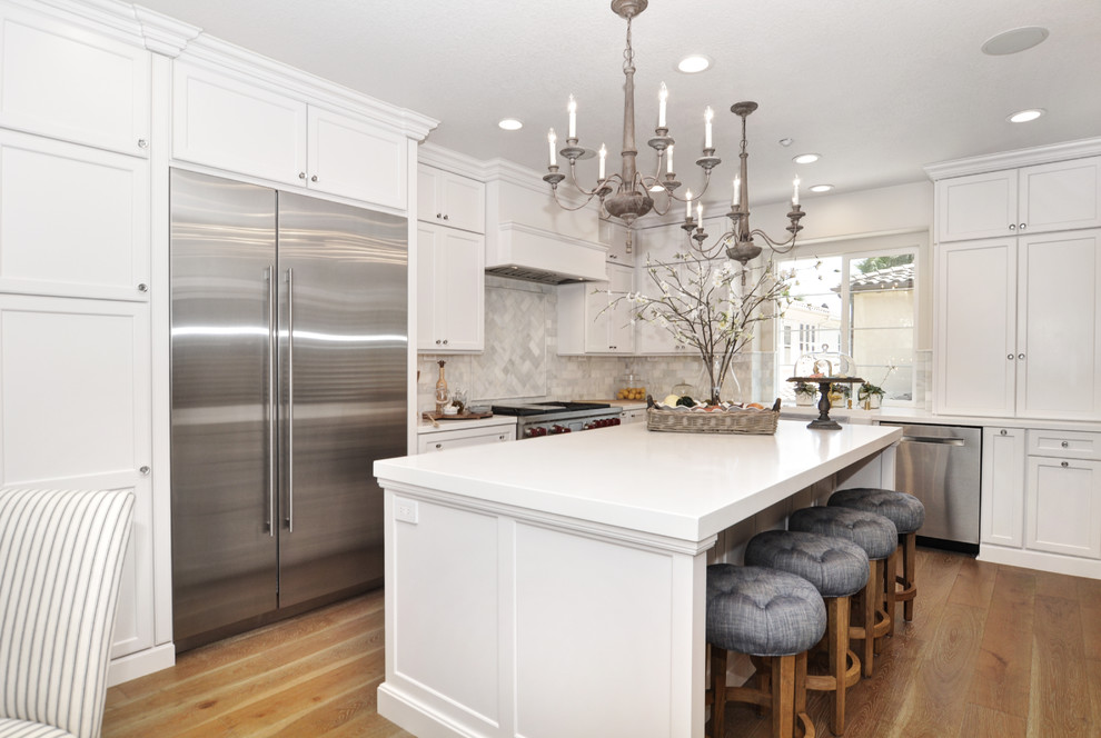 Inspiration for a transitional l-shaped kitchen in Orange County with shaker cabinets, white cabinets, grey splashback, stainless steel appliances, medium hardwood floors, with island, brown floor and white benchtop.