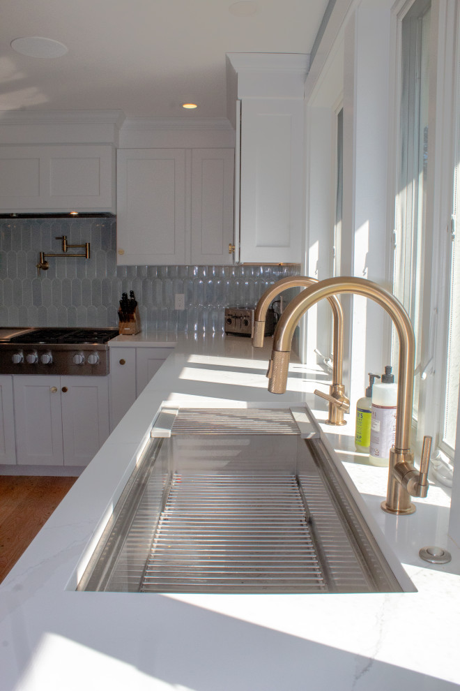 Bild på ett mycket stort funkis vit vitt kök, med en undermonterad diskho, släta luckor, vita skåp, bänkskiva i kvartsit, blått stänkskydd, rostfria vitvaror, mellanmörkt trägolv, flera köksöar och brunt golv