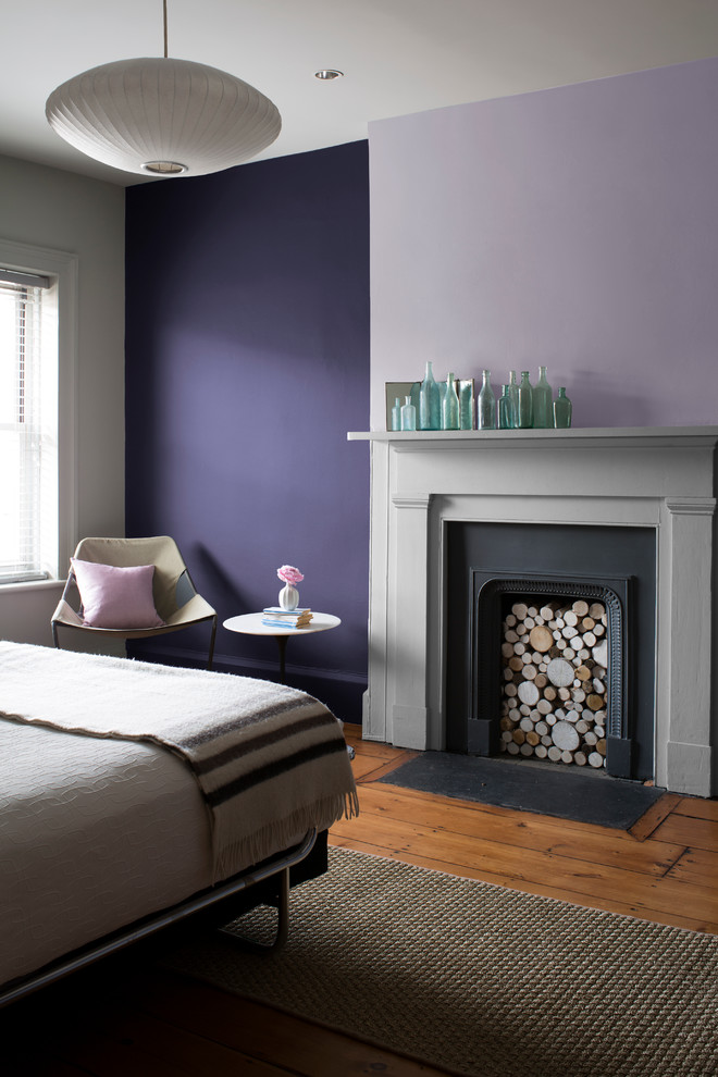 Photo of a bedroom in Vancouver with purple walls, medium hardwood floors, a standard fireplace and a plaster fireplace surround.