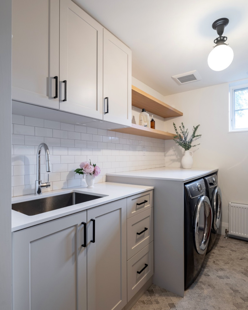 Design ideas for a medium sized classic galley separated utility room in Toronto with a submerged sink, recessed-panel cabinets, grey cabinets, engineered stone countertops, white splashback, ceramic splashback, white walls, a side by side washer and dryer, grey floors and grey worktops.