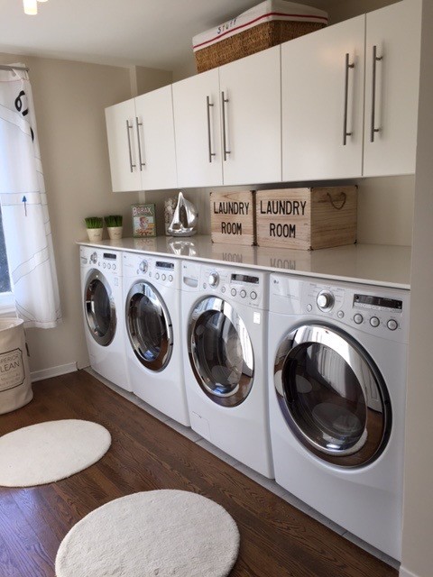 Inspiration for an expansive contemporary single-wall dedicated laundry room in Montreal with flat-panel cabinets, white cabinets, solid surface benchtops, white walls, dark hardwood floors and a side-by-side washer and dryer.
