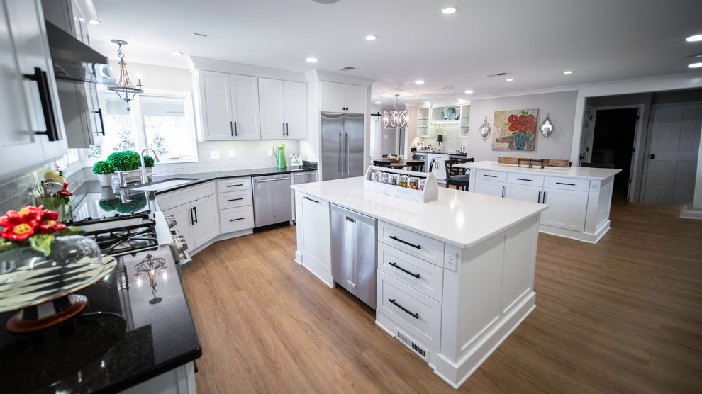 Eat-in kitchen - large modern l-shaped medium tone wood floor and brown floor eat-in kitchen idea with an undermount sink, recessed-panel cabinets, white cabinets, solid surface countertops, gray backsplash, stainless steel appliances, two islands and multicolored countertops