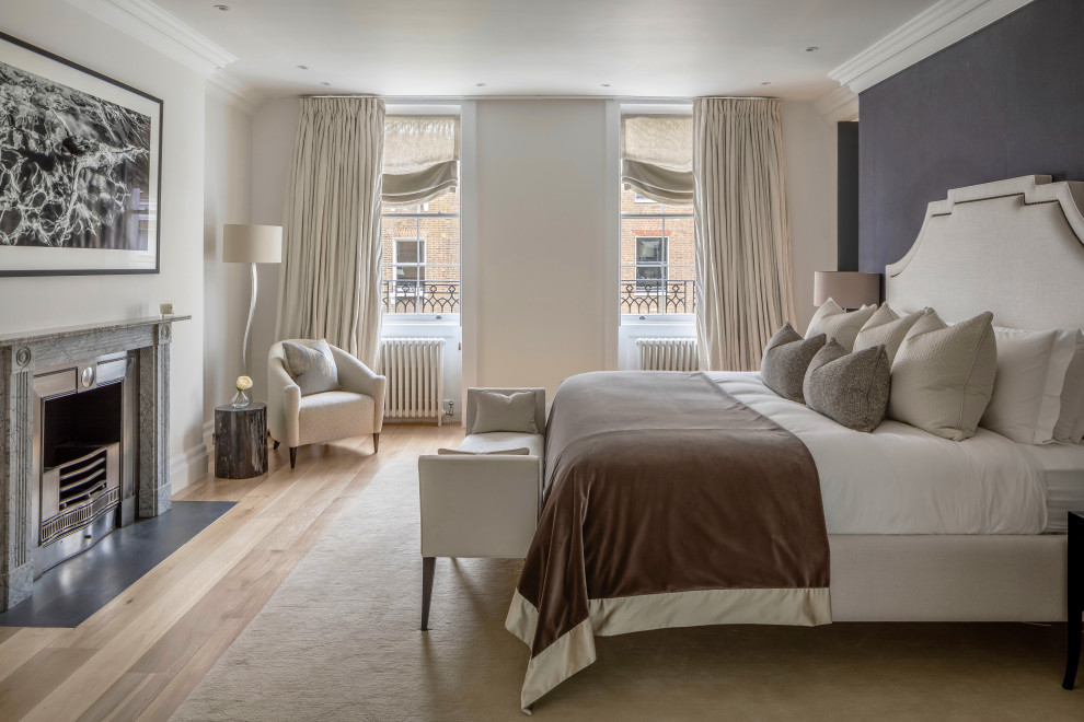 Design ideas for a large classic master bedroom in London with white walls, light hardwood flooring, a standard fireplace, a stone fireplace surround, beige floors, wallpapered walls and a chimney breast.