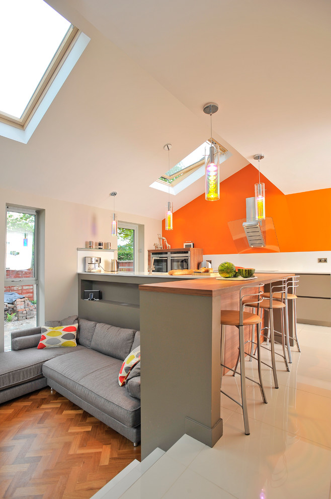 This is an example of a contemporary l-shaped kitchen in Manchester with flat-panel cabinets, stainless steel appliances, a peninsula, wood benchtops and orange splashback.