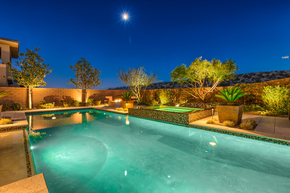 Photo of a large tropical backyard rectangular lap pool in Las Vegas with a hot tub and natural stone pavers.