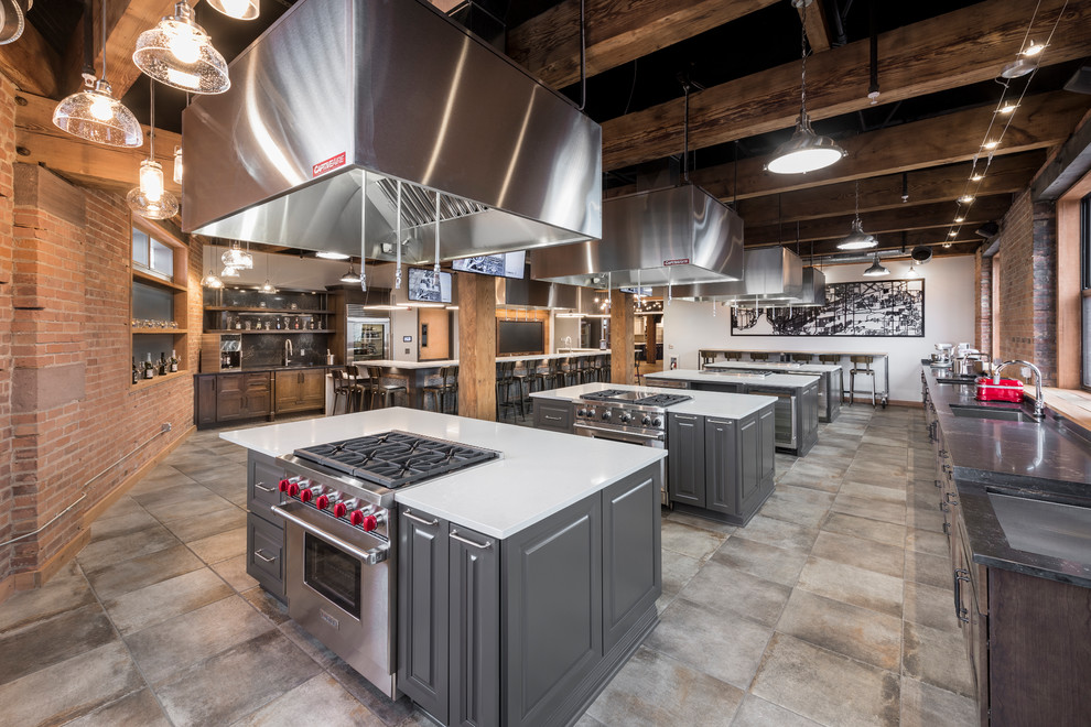 This is an example of an expansive industrial u-shaped eat-in kitchen in New York with an undermount sink, raised-panel cabinets, grey cabinets, quartz benchtops, grey splashback, glass tile splashback, stainless steel appliances, ceramic floors, multiple islands, beige floor and white benchtop.