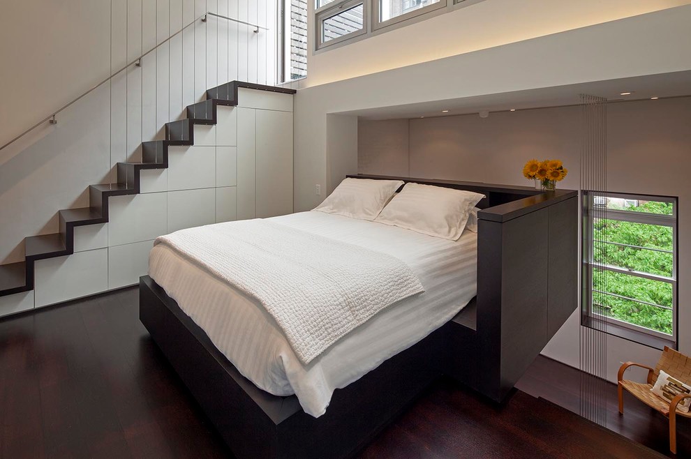 Photo of a small modern loft-style bedroom in New York with white walls, dark hardwood floors and no fireplace.