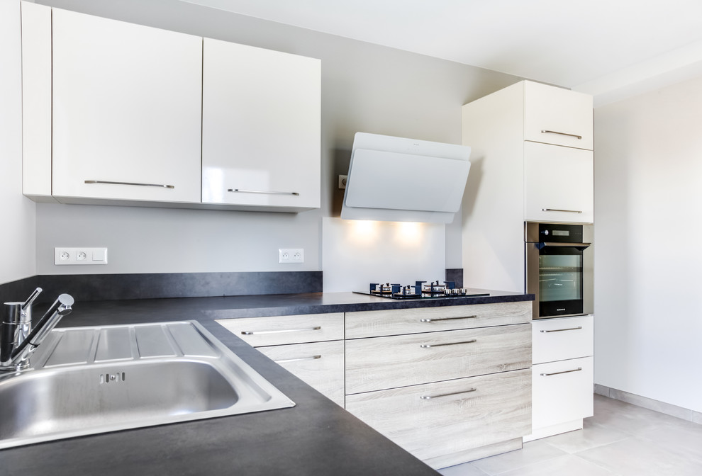 This is an example of a small contemporary u-shaped separate kitchen in Toulouse with a single-bowl sink, laminate benchtops, black splashback, glass sheet splashback, white appliances, ceramic floors, no island and beige floor.