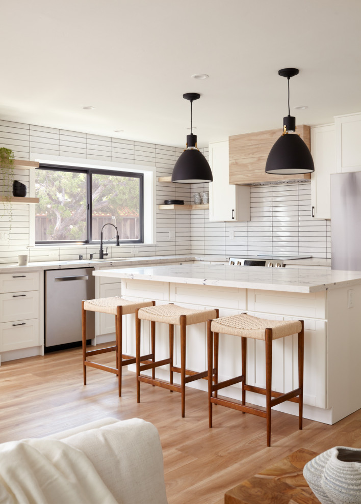 Photo of a transitional l-shaped open plan kitchen in San Francisco with an undermount sink, shaker cabinets, white cabinets, white splashback, stainless steel appliances, medium hardwood floors, with island, brown floor and white benchtop.