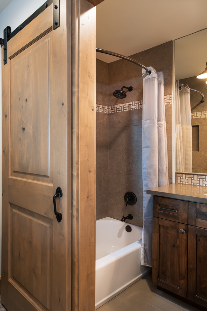 Photo of a mid-sized country kids bathroom in Other with recessed-panel cabinets, dark wood cabinets, a drop-in tub, a shower/bathtub combo, a one-piece toilet, gray tile, ceramic tile, beige walls, ceramic floors, an undermount sink and quartzite benchtops.