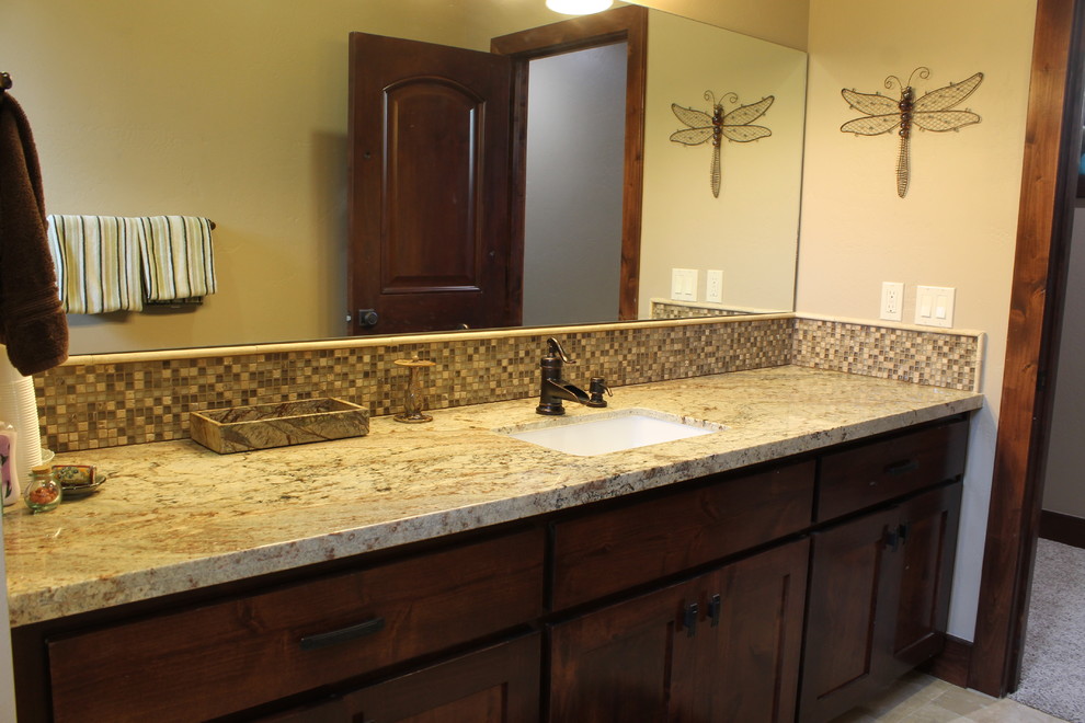 This is an example of a mid-sized country kids bathroom in San Luis Obispo with recessed-panel cabinets, dark wood cabinets, granite benchtops, stone tile, beige tile, brown tile, beige walls, ceramic floors and an undermount sink.