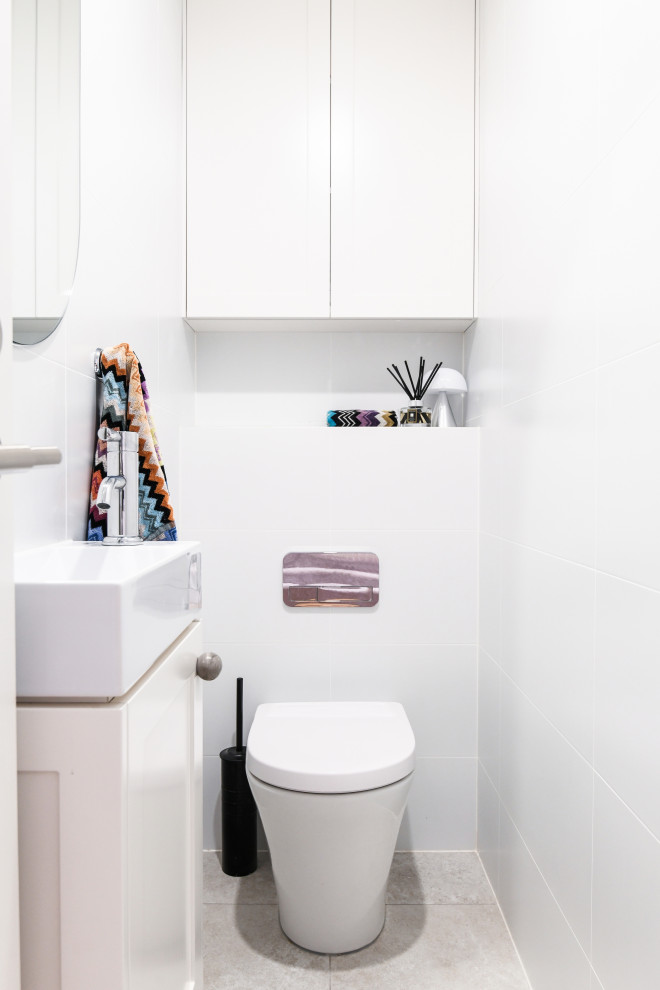 Klassisk inredning av ett litet toalett, med vita skåp, en toalettstol med hel cisternkåpa, vit kakel, keramikplattor, vita väggar, klinkergolv i keramik, ett fristående handfat och beiget golv