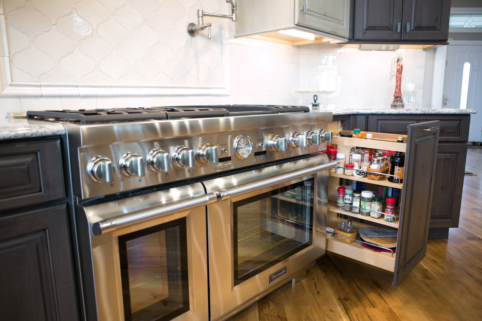 Kitchen - large transitional u-shaped medium tone wood floor and brown floor kitchen idea in Indianapolis with a farmhouse sink, raised-panel cabinets, dark wood cabinets, granite countertops, white backsplash, subway tile backsplash, paneled appliances, an island and multicolored countertops
