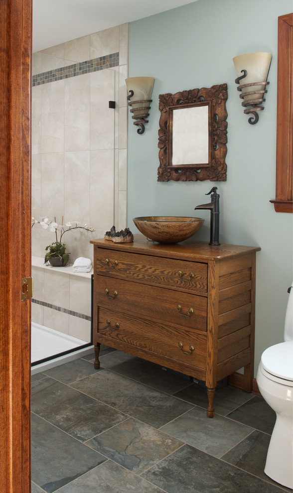 Inspiration for a mid-sized eclectic bathroom in New York with a vessel sink, furniture-like cabinets, medium wood cabinets, wood benchtops, an alcove shower, a two-piece toilet, beige tile, ceramic tile, blue walls and slate floors.