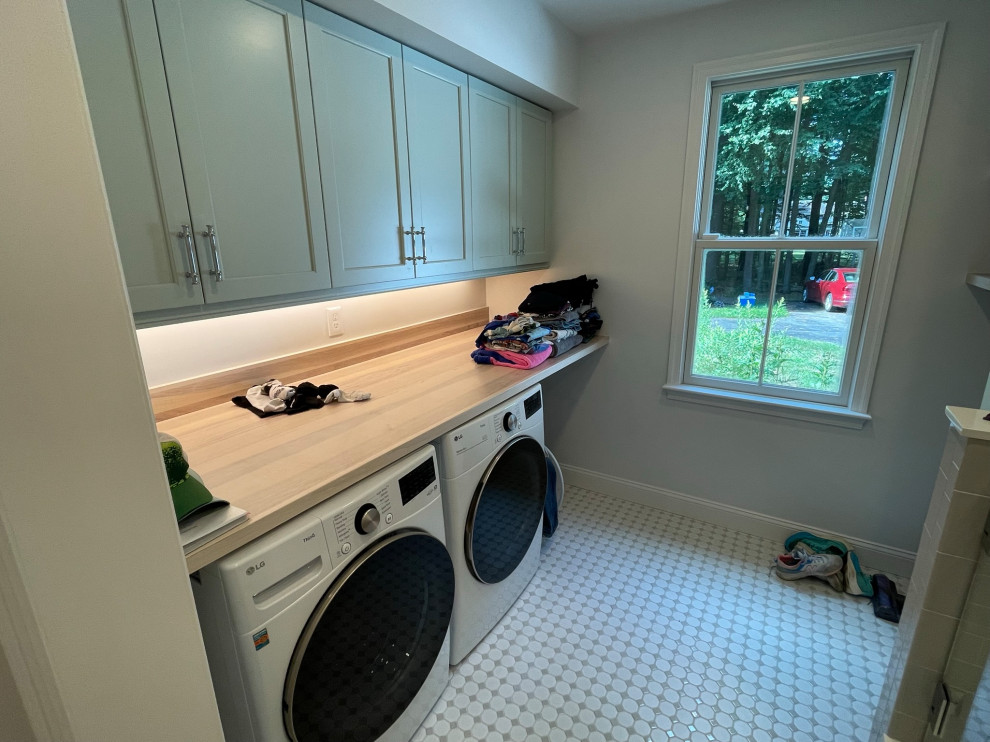 Photo of a mid-sized modern utility room in Boston with shaker cabinets, green cabinets, wood benchtops, white walls, ceramic floors, a side-by-side washer and dryer, grey floor and brown benchtop.