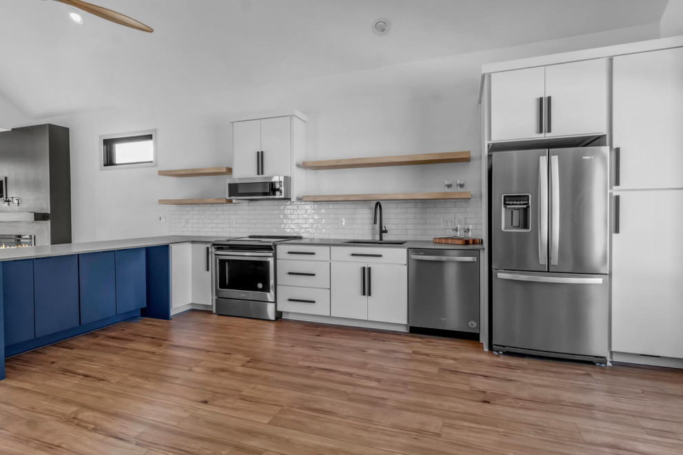 Photo of a mid-sized modern single-wall eat-in kitchen in New York with an undermount sink, flat-panel cabinets, white cabinets, quartz benchtops, white splashback, subway tile splashback, stainless steel appliances, light hardwood floors, a peninsula, beige floor and grey benchtop.