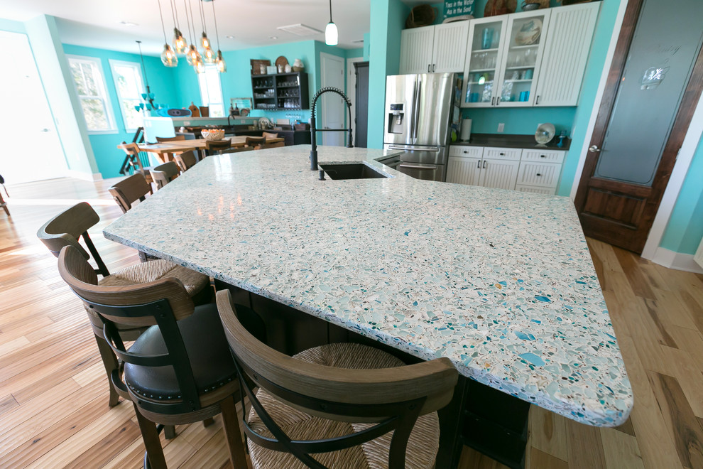 This is an example of a large beach style l-shaped open plan kitchen in Charleston with an undermount sink, white cabinets, recycled glass benchtops, blue splashback, black appliances, dark hardwood floors and with island.