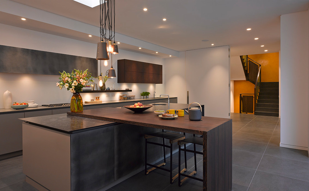 This is an example of a large contemporary single-wall open plan kitchen in London with flat-panel cabinets, grey cabinets, quartzite benchtops, white splashback, glass sheet splashback, panelled appliances, ceramic floors, with island, grey floor and grey benchtop.