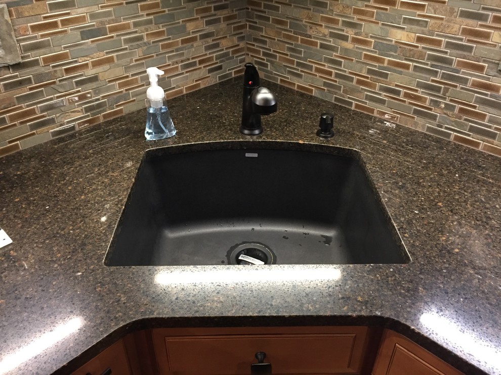 Example of a small mountain style u-shaped light wood floor kitchen design with a single-bowl sink, raised-panel cabinets, brown cabinets, quartz countertops and mosaic tile backsplash