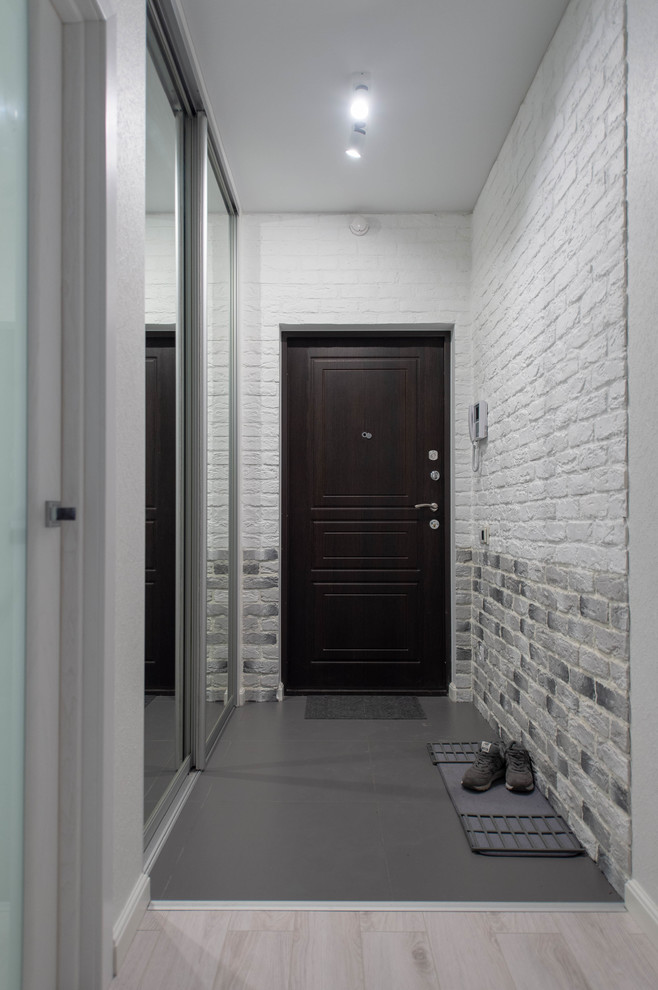 This is an example of a small contemporary front door in Saint Petersburg with white walls, porcelain floors, a dark wood front door and grey floor.