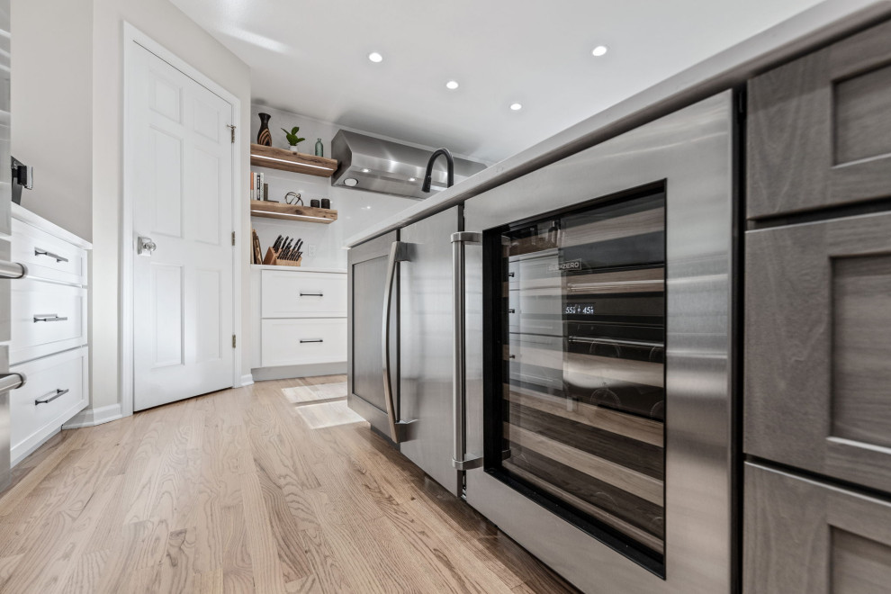 Inspiration for a large transitional u-shaped light wood floor and multicolored floor eat-in kitchen remodel with a single-bowl sink, shaker cabinets, white cabinets, quartz countertops, white backsplash, quartz backsplash, stainless steel appliances, an island and white countertops
