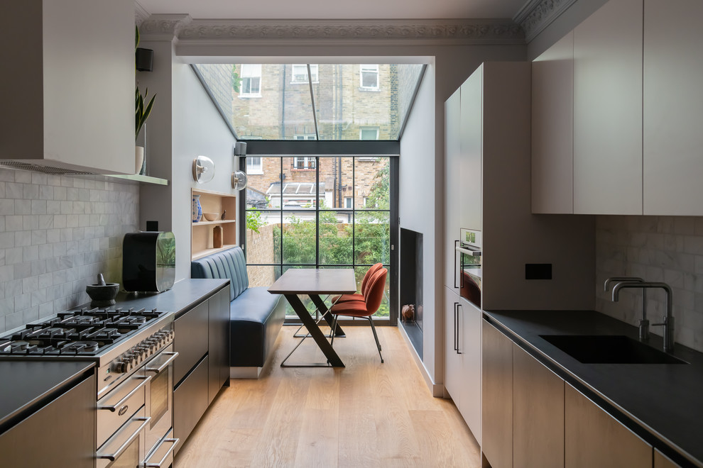 Inspiration for a contemporary galley eat-in kitchen in London with an integrated sink, flat-panel cabinets, grey cabinets, grey splashback, stainless steel appliances, medium hardwood floors, no island and black benchtop.