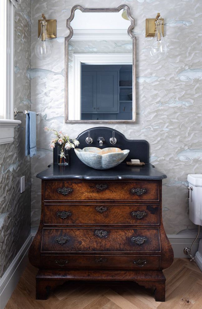 Inspiration for a large traditional powder room in San Francisco with furniture-like cabinets, dark wood cabinets, grey walls, a vessel sink, brown floor, black benchtops, medium hardwood floors, a freestanding vanity and wallpaper.