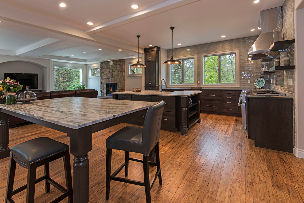 Example of a large transitional l-shaped medium tone wood floor and brown floor open concept kitchen design with a farmhouse sink, shaker cabinets, dark wood cabinets, granite countertops, gray backsplash, subway tile backsplash, paneled appliances and an island