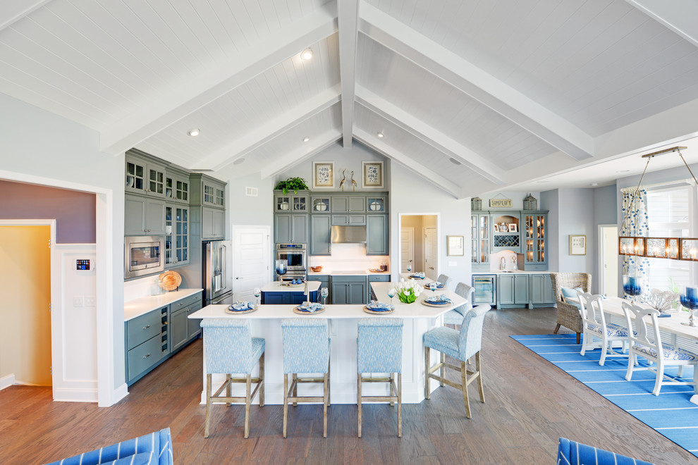 Inspiration for a beach style eat-in kitchen in Other with recessed-panel cabinets, grey cabinets, quartz benchtops, white splashback, ceramic splashback, stainless steel appliances, medium hardwood floors, with island and a farmhouse sink.