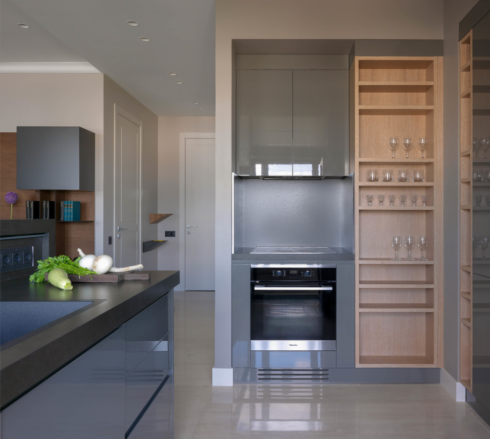Mid-sized contemporary l-shaped open plan kitchen in Other with flat-panel cabinets, grey cabinets, grey splashback, porcelain splashback, black appliances, marble floors, a peninsula, beige floor, black benchtop, a drop-in sink and granite benchtops.