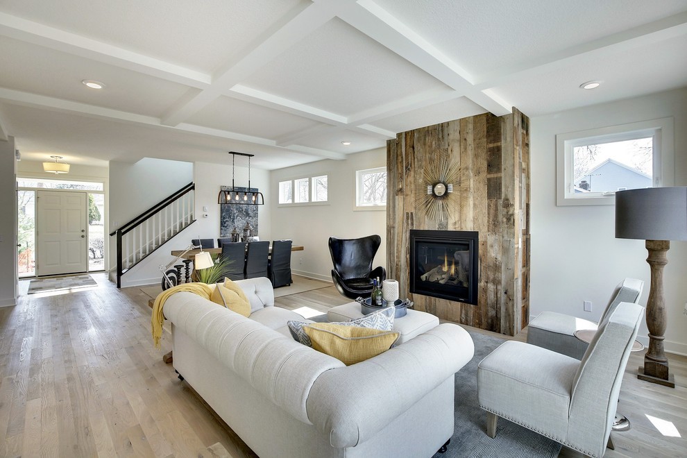 Design ideas for a large country open concept living room in Minneapolis with white walls, light hardwood floors, a standard fireplace, a wood fireplace surround and a wall-mounted tv.