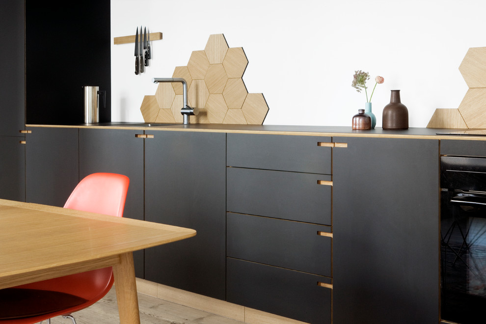 This is an example of a mid-sized scandinavian single-wall eat-in kitchen in Copenhagen with a drop-in sink, flat-panel cabinets, black cabinets, laminate benchtops, mosaic tile splashback, light hardwood floors and with island.