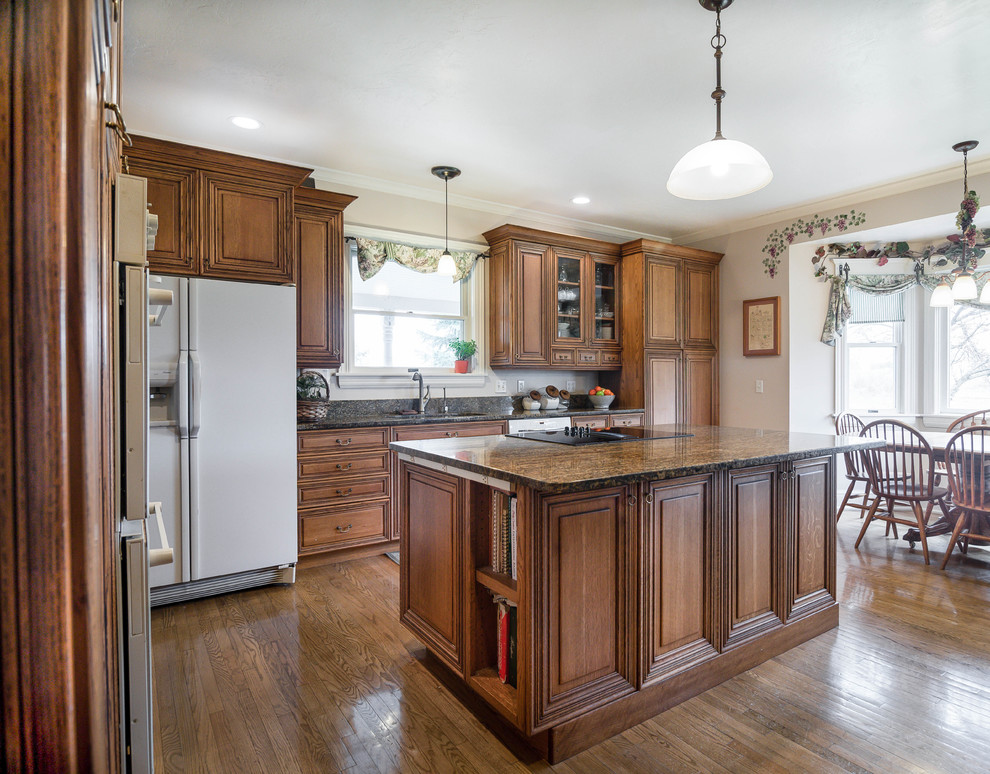 Traditional l-shaped kitchen in Salt Lake City with an undermount sink, raised-panel cabinets, medium wood cabinets, granite benchtops, white appliances, medium hardwood floors, with island and multi-coloured benchtop.