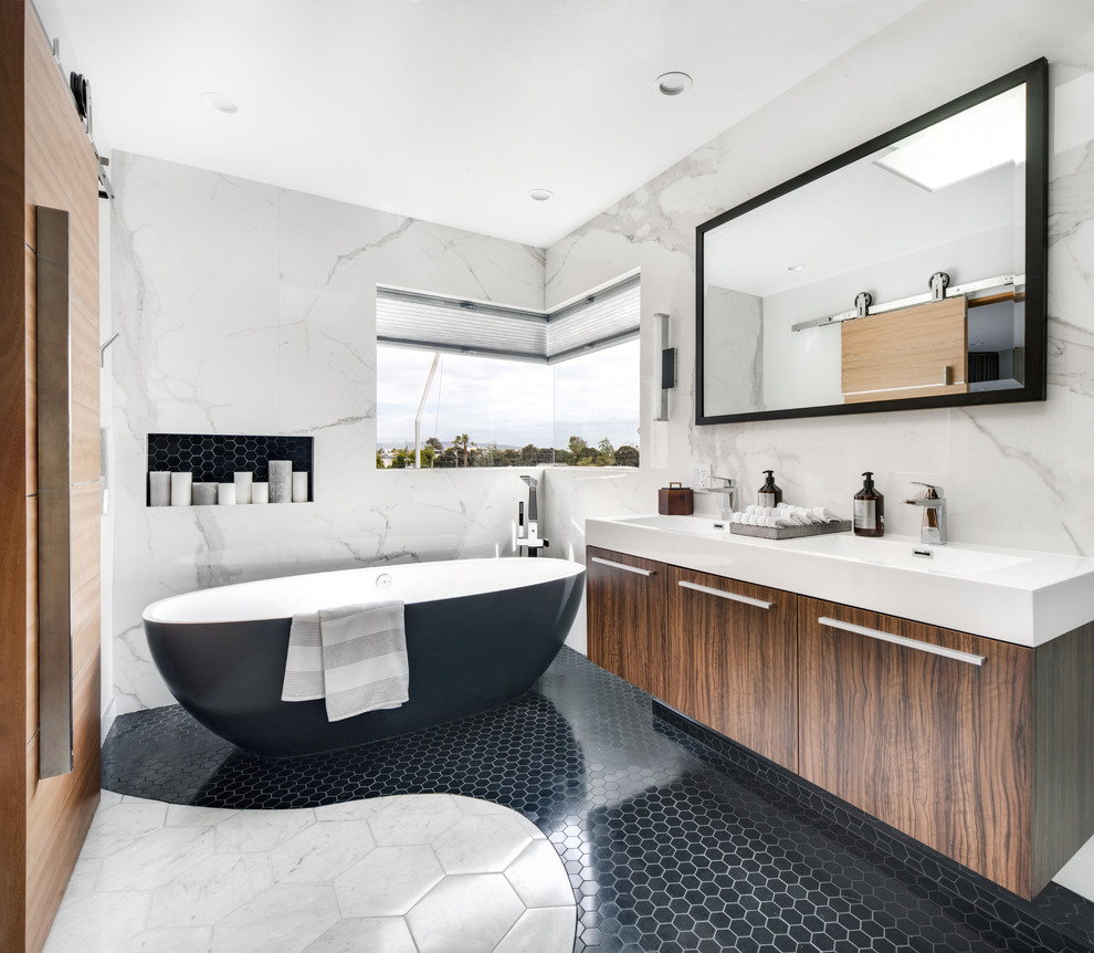 Photo of a mid-sized modern master bathroom in Orange County with flat-panel cabinets, medium wood cabinets, a freestanding tub, a corner shower, a two-piece toilet, white tile, stone slab, white walls, marble floors, an integrated sink, engineered quartz benchtops, white floor, a hinged shower door and white benchtops.