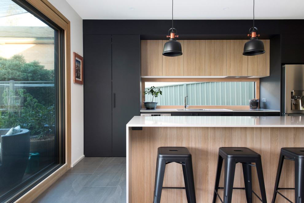 Inspiration for a mid-sized contemporary galley open plan kitchen in Canberra - Queanbeyan with an undermount sink, flat-panel cabinets, light wood cabinets, quartz benchtops, multi-coloured splashback, glass sheet splashback, stainless steel appliances, porcelain floors, with island, grey floor and white benchtop.