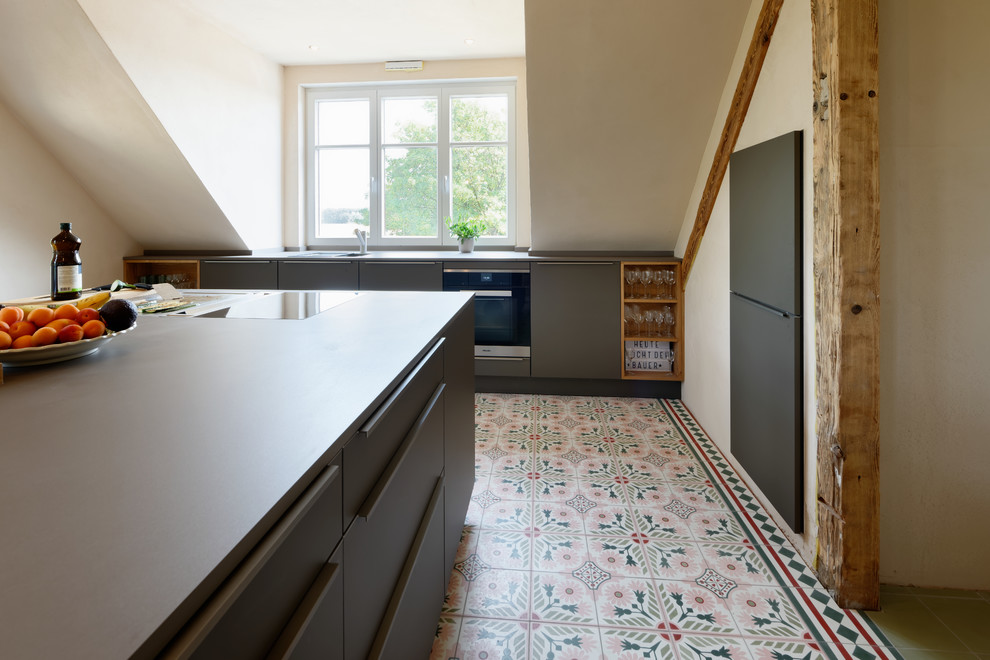 Photo of a contemporary galley open plan kitchen in Essen with a drop-in sink, flat-panel cabinets, black cabinets, black appliances, ceramic floors, with island, multi-coloured floor and black benchtop.