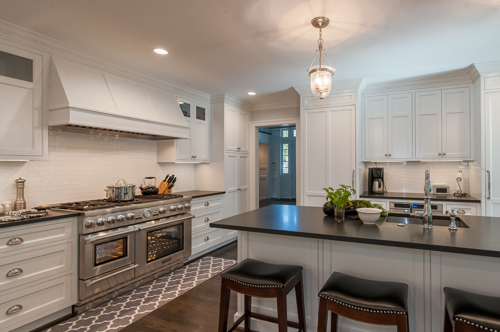 Inspiration for a large traditional l-shaped open plan kitchen in DC Metro with a farmhouse sink, recessed-panel cabinets, white cabinets, quartz benchtops, white splashback, ceramic splashback, stainless steel appliances, dark hardwood floors, with island and brown floor.