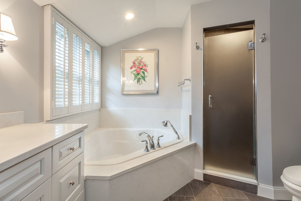 Photo of a mid-sized traditional master bathroom in DC Metro with raised-panel cabinets, white cabinets, a corner tub, a corner shower, a two-piece toilet, gray tile, porcelain tile, grey walls, porcelain floors, an undermount sink, marble benchtops, grey floor, a hinged shower door and white benchtops.