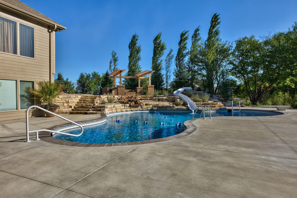 Large mountain style backyard concrete paver and custom-shaped water slide photo in Omaha
