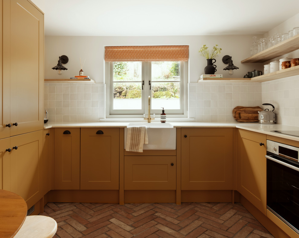 Design ideas for a small bohemian u-shaped kitchen/diner in Cornwall with a belfast sink, shaker cabinets, yellow cabinets, quartz worktops, white splashback, ceramic splashback, stainless steel appliances, terracotta flooring, no island, brown floors, white worktops and feature lighting.