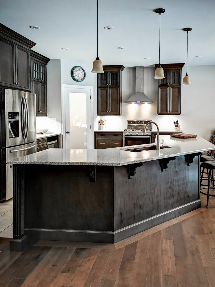 Photo of a mid-sized country l-shaped eat-in kitchen in Other with a double-bowl sink, recessed-panel cabinets, dark wood cabinets, granite benchtops, stainless steel appliances, medium hardwood floors, with island, brown floor and grey benchtop.
