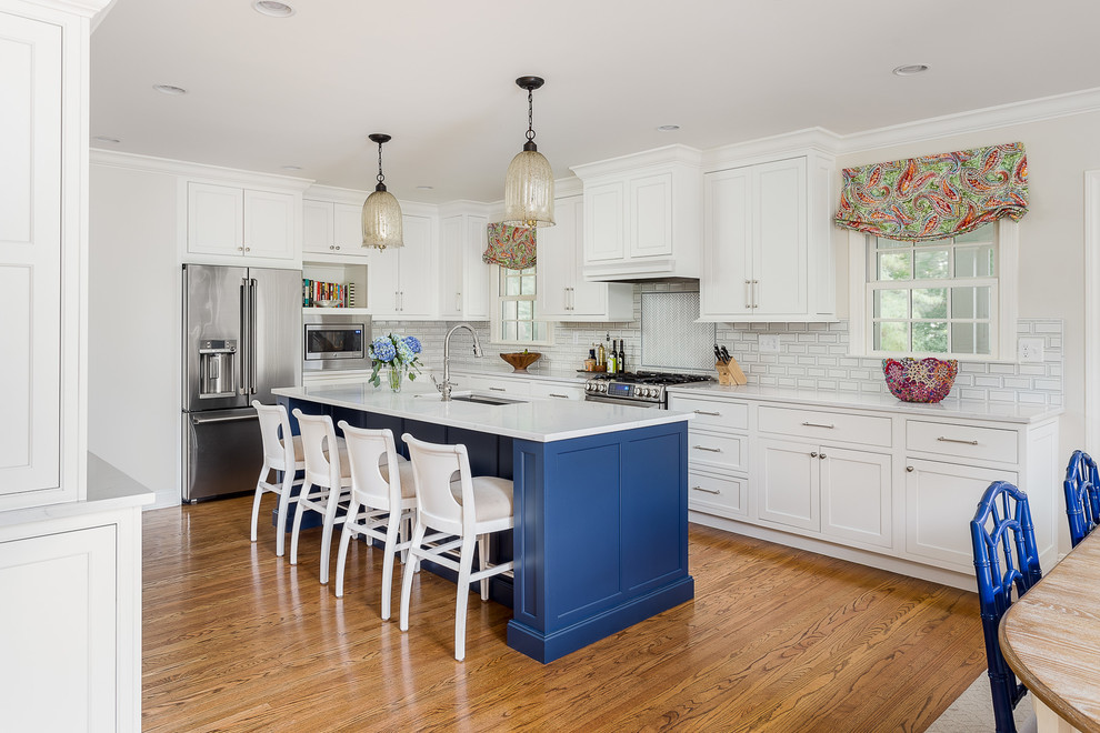 This is an example of a mid-sized beach style galley eat-in kitchen in Louisville with a single-bowl sink, flat-panel cabinets, white cabinets, quartz benchtops, white splashback, ceramic splashback, stainless steel appliances, light hardwood floors, with island, brown floor and white benchtop.