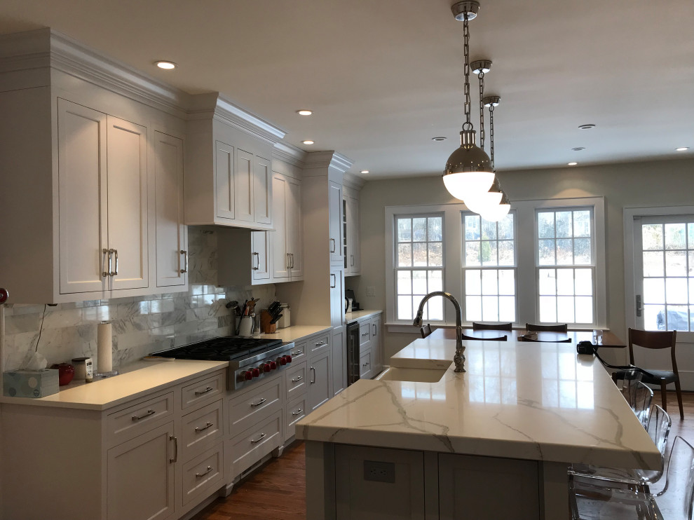 Large transitional u-shaped medium tone wood floor and brown floor eat-in kitchen photo with a farmhouse sink, recessed-panel cabinets, white cabinets, quartz countertops, white backsplash, subway tile backsplash, stainless steel appliances, an island and white countertops
