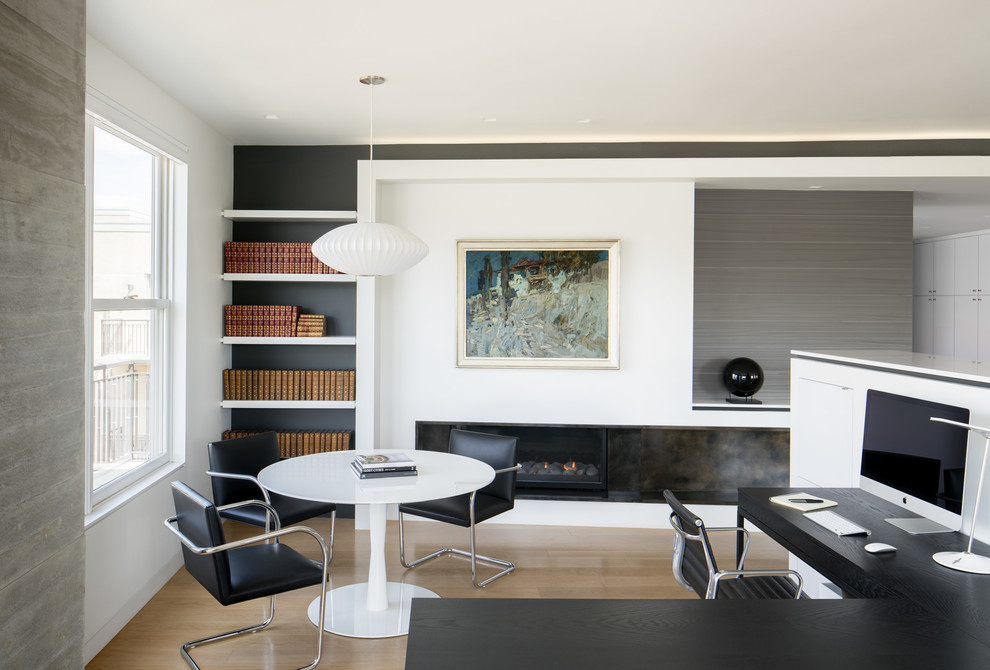 Photo of a mid-sized modern study room in Denver with white walls, light hardwood floors, a standard fireplace, a metal fireplace surround, a freestanding desk and brown floor.