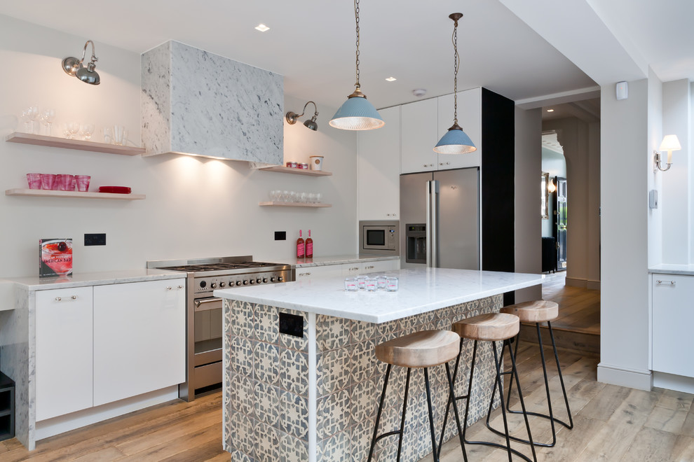 Inspiration for a contemporary galley kitchen in London with flat-panel cabinets, white cabinets, stainless steel appliances, light hardwood floors and with island.