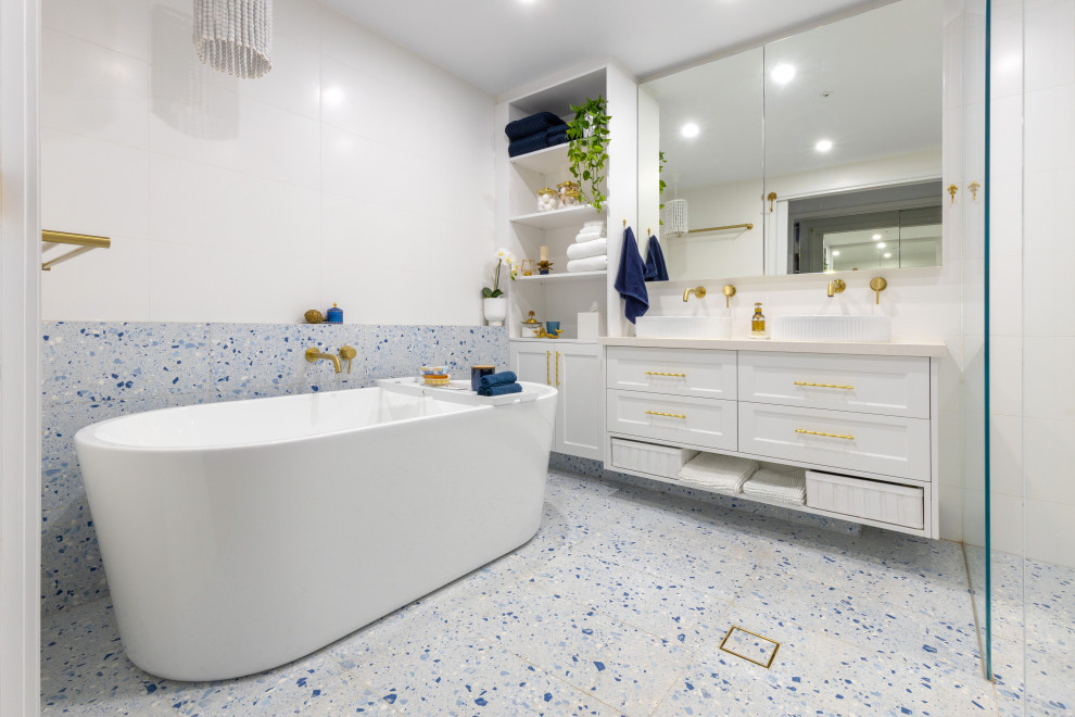 Идея дизайна: большая главная ванная комната в стиле модернизм с фасадами с филенкой типа жалюзи, белыми фасадами, отдельно стоящей ванной, открытым душем, инсталляцией, белой плиткой, керамогранитной плиткой, белыми стенами, полом из керамогранита, настольной раковиной, столешницей из искусственного кварца, синим полом, открытым душем, белой столешницей, нишей, тумбой под две раковины и подвесной тумбой