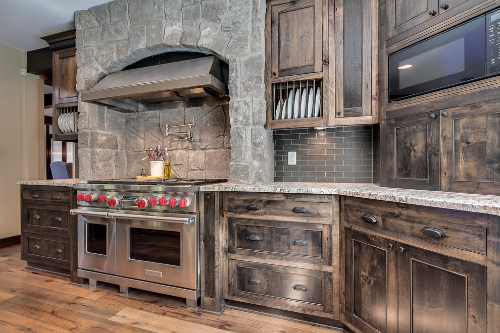 Inspiration for a large country l-shaped open plan kitchen in Portland with a farmhouse sink, recessed-panel cabinets, dark wood cabinets, granite benchtops, brown splashback, glass tile splashback, stainless steel appliances and medium hardwood floors.