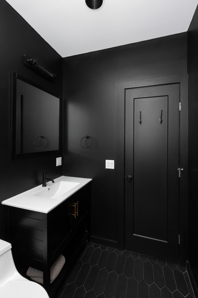 This is an example of a mid-sized industrial 3/4 bathroom in New York with an alcove shower, a one-piece toilet, gray tile, cement tiles, an open shower, black cabinets, black walls, an integrated sink, solid surface benchtops, black floor, white benchtops, subway tile and recessed-panel cabinets.