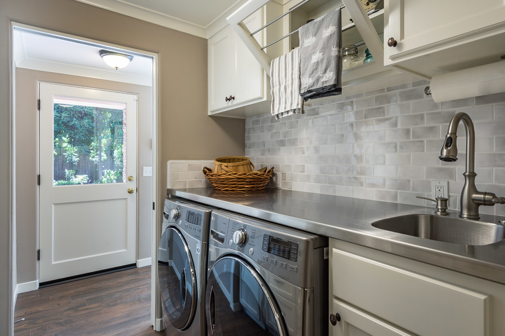 Photo of a small contemporary galley dedicated laundry room in Other with an utility sink, shaker cabinets, white cabinets, grey walls, dark hardwood floors, a side-by-side washer and dryer, brown floor, white benchtop and stainless steel benchtops.
