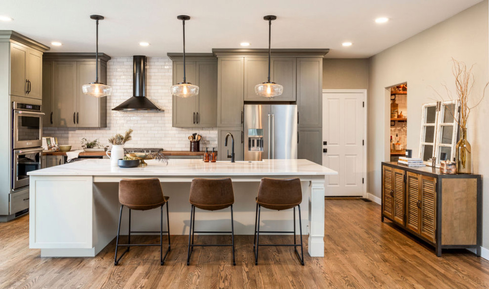 Inspiration for a large transitional l-shaped open plan kitchen in Denver with an undermount sink, shaker cabinets, grey cabinets, quartz benchtops, white splashback, ceramic splashback, stainless steel appliances, medium hardwood floors, with island, brown floor and white benchtop.